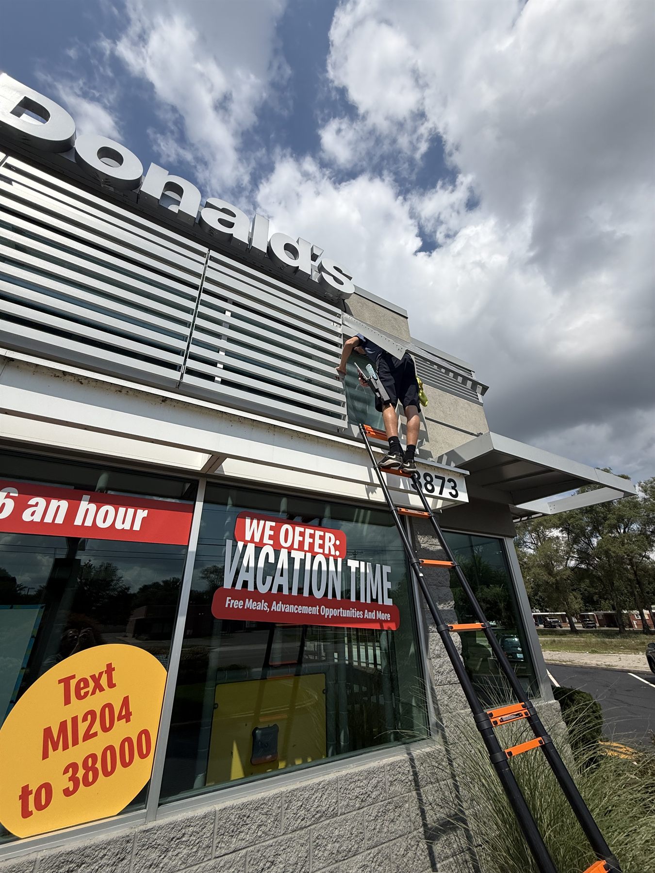 Team Gleam crew member on a ladder cleaning high exterior windows on a commercial building